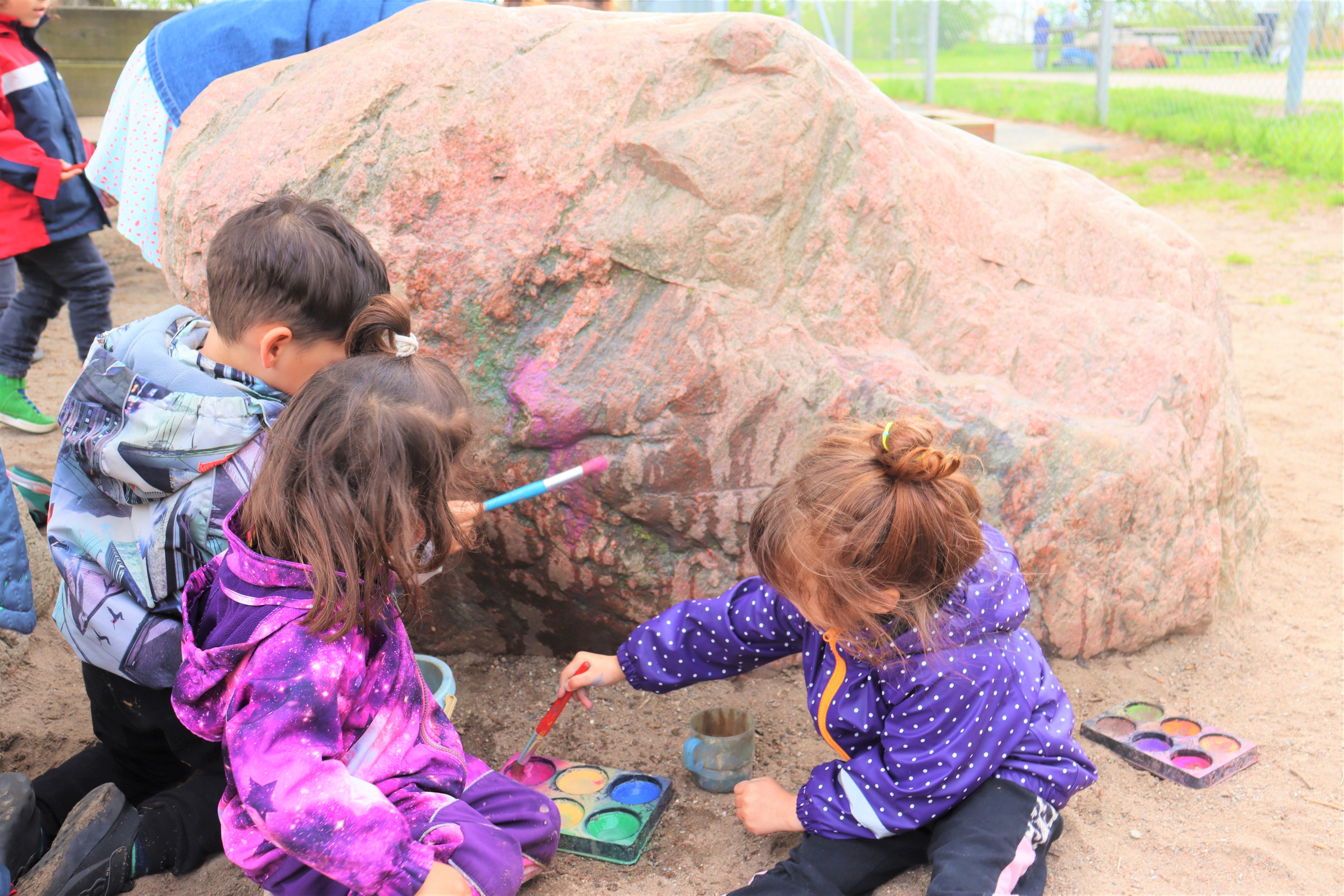 Børn maler på stor sten med vandmaling